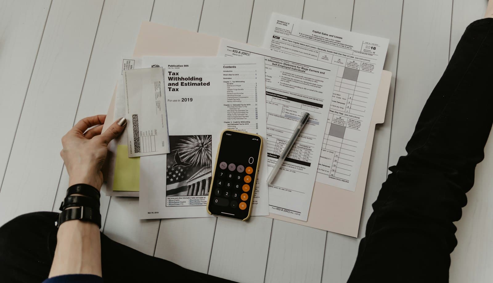 Hands sorting tax withholding forms beside a calculator
