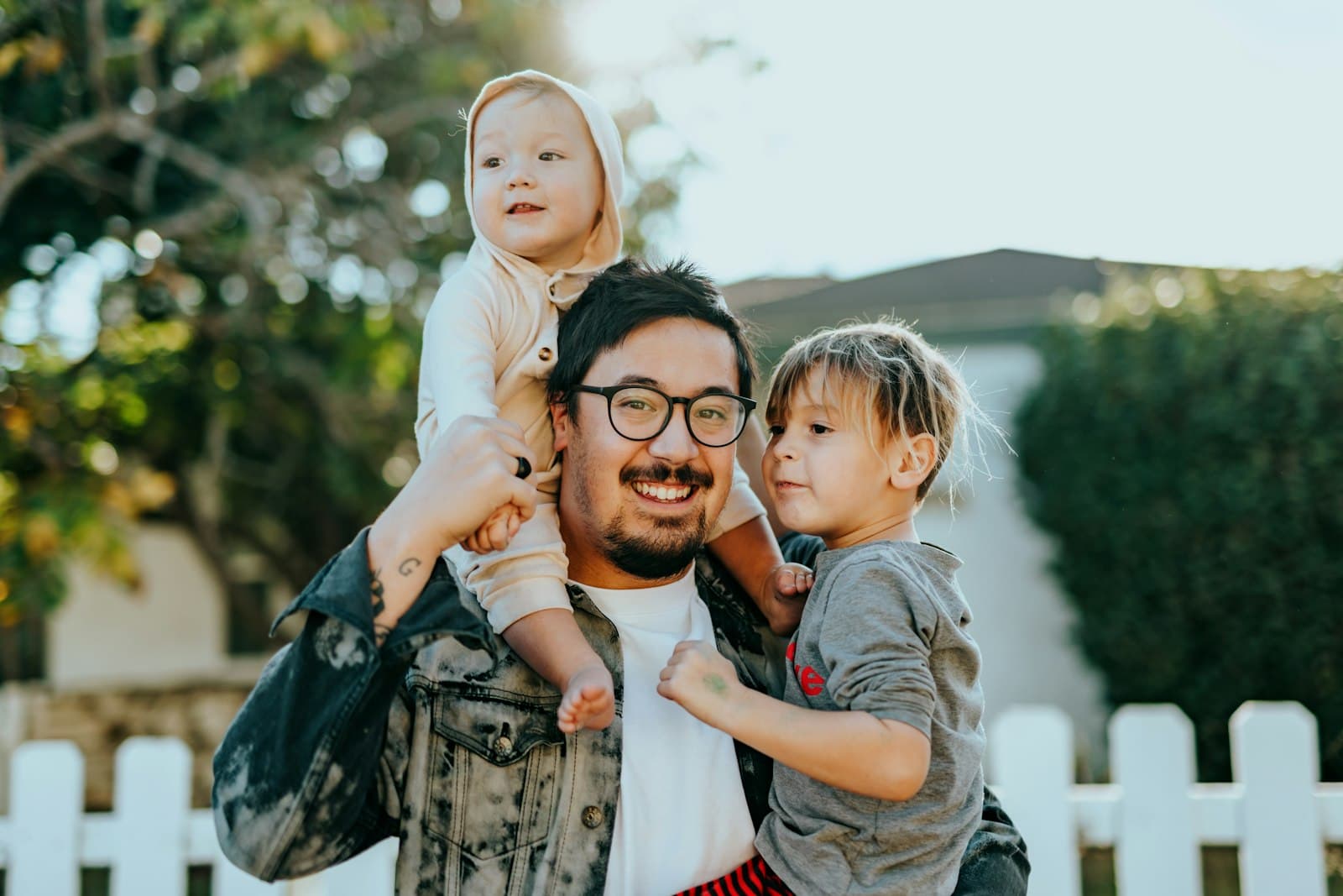 Smiling father carrying his two young children outside their home