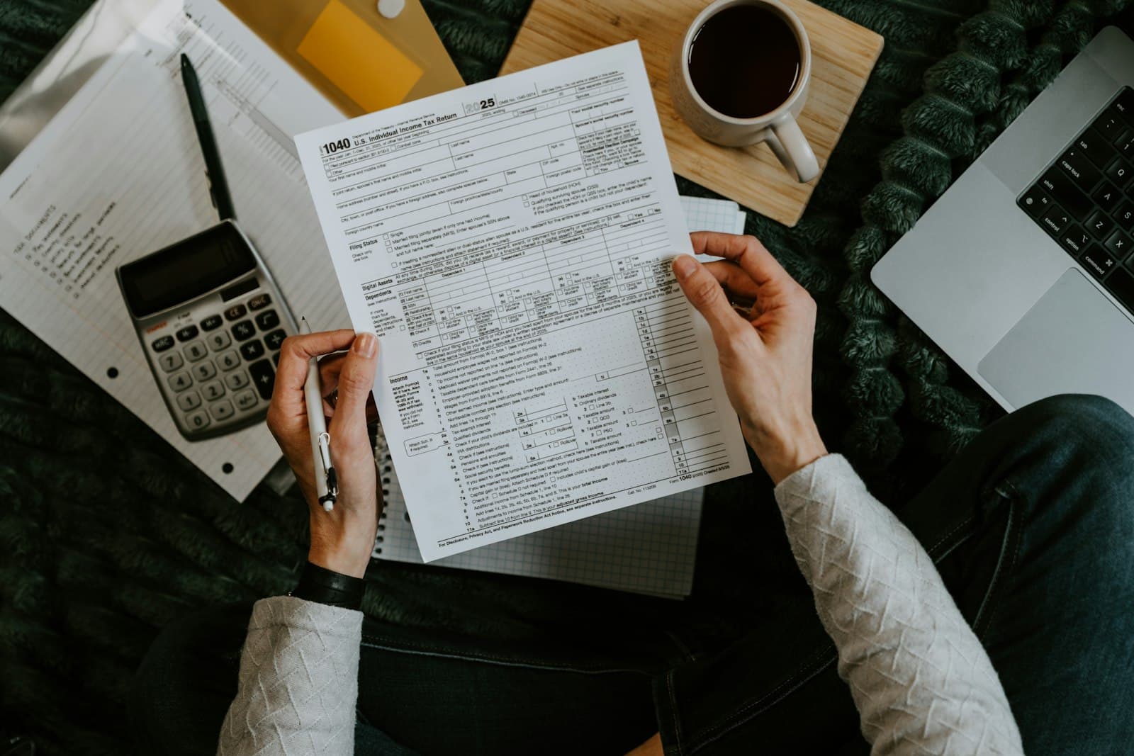 Hands holding a Form 1040 beside a calculator and laptop